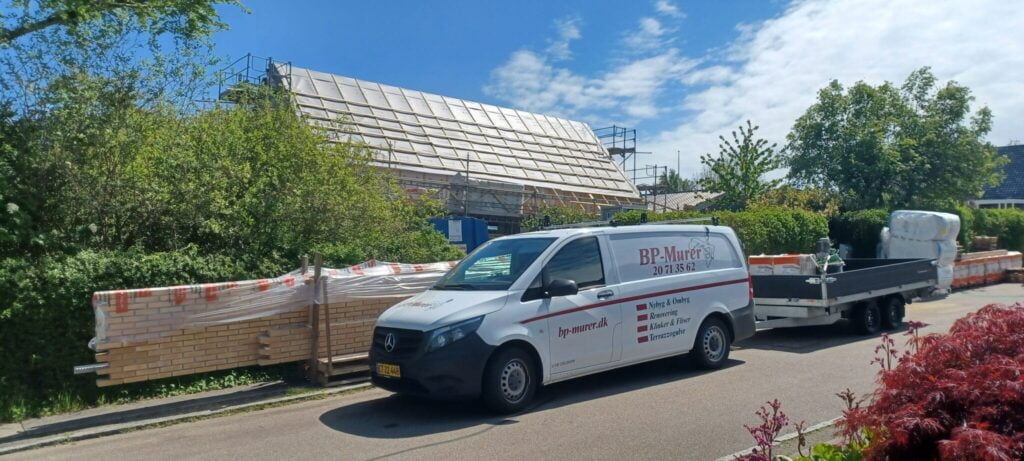 Husbyggeri med murerbil og byggematerialer på gaden
