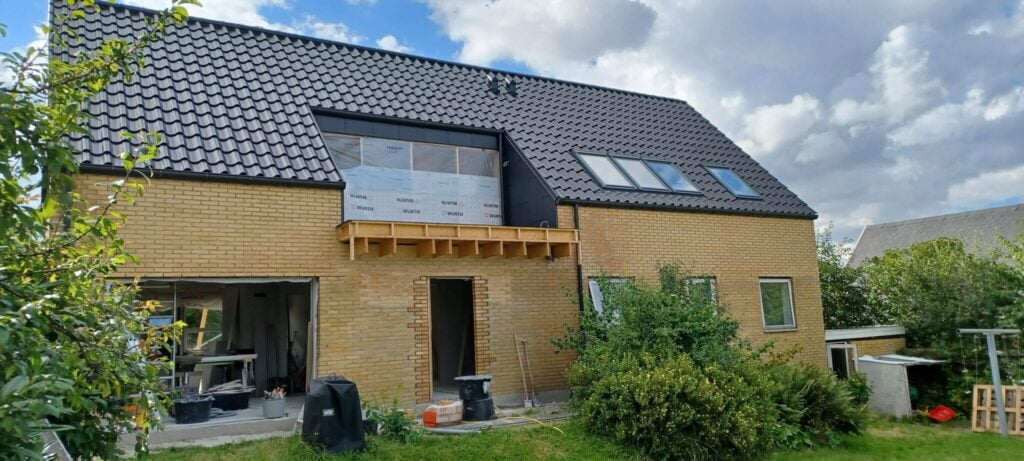 Gult murstenshus under renovering med sort tag